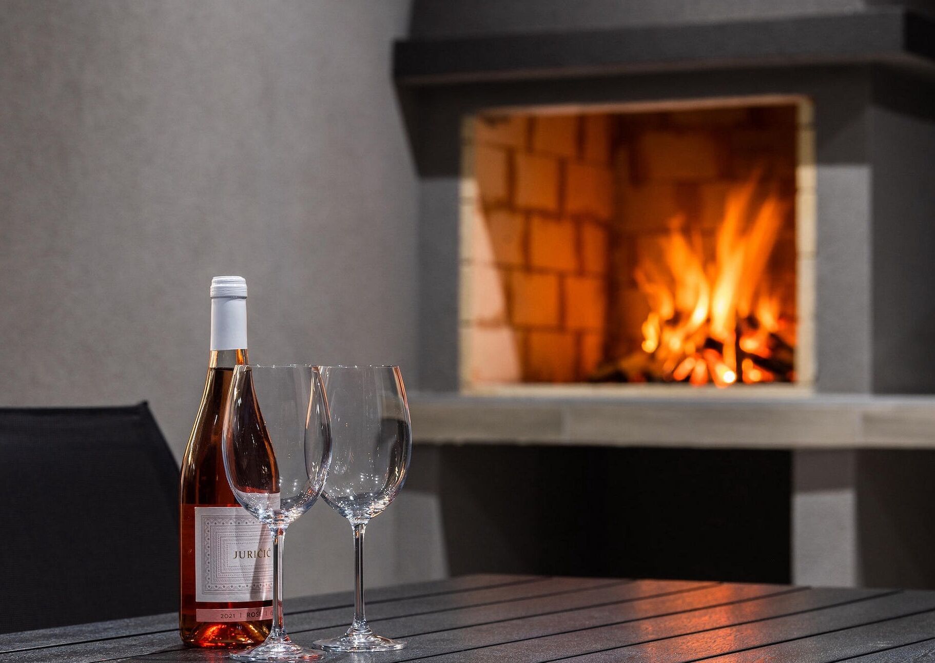 Una botella de vino y dos copas sobre una mesa, con una chimenea al fondo.