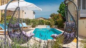 Uma área junto à piscina com duas cadeiras suspensas, um guarda-sol branco e uma piscina.