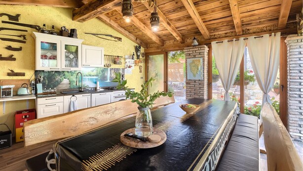 Cozinha rústica com vigas de madeira, bancada preta e vista para o exterior.