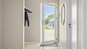 Ein Flur mit einer zur Außenwelt führenden Tür, einem Kleiderständer mit Kleidung und einem kleinen Haus im Hintergrund.