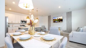 Un salon moderne comprenant un coin repas, des meubles blancs et un téléviseur à écran plat fixé au mur.