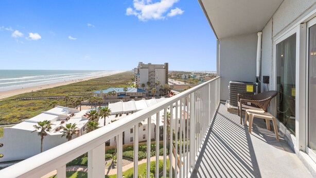 A balcony with a view of the beach, a pool area, and a building with multiple stories in the background. - Ocean Views from Aquarius 806! 2 BD 1BA for 4 people (South Padre Island)