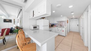 A modern kitchen with white cabinetry, a central island, and a dining area with wooden chairs. - Ocean Views from Aquarius 806! 2 BD 1BA for 4 people (South Padre Island)