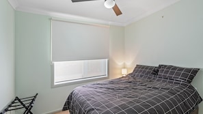 Une chambre à coucher avec un lit, une fenêtre avec des stores, un ventilateur de plafond et une lampe de chevet.