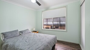 A bedroom with a bed, a nightstand, a window with a view of the outside, and a ceiling light.