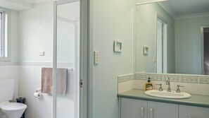 A bathroom with a toilet, a shower, a sink with a mirror, and a towel rack.