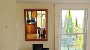 A room with a leather chair, a table, a fireplace, a window with a view of greenery, and a mirror on the wall.