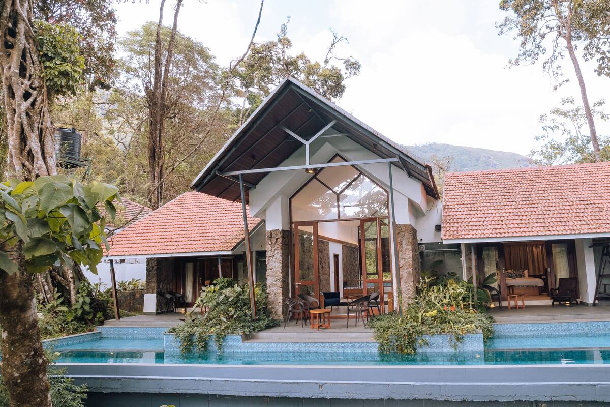 A two-story house with a swimming pool, surrounded by trees and a mountain in the background.