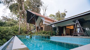 A swimming pool with a tiled edge, surrounded by lush greenery and trees. - ELIXIR WOODS RESORT AND SPA (Devikolam)