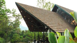 A building with a sloped roof, a paved entrance, and surrounding greenery. - ELIXIR WOODS RESORT AND SPA (Devikolam)