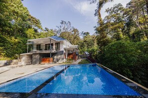 A modern house with a swimming pool, surrounded by lush greenery and trees. - ELIXIR WOODS RESORT AND SPA (Devikolam)