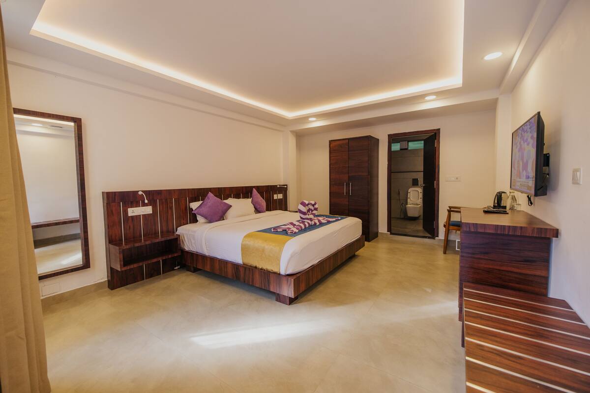 A modern hotel room with a wooden bed, a desk, and a bathroom visible through an open door.