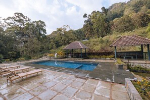 A swimming pool with lounge chairs, a gazebo, and a stone patio. - ELIXIR WOODS RESORT AND SPA (Devikolam)