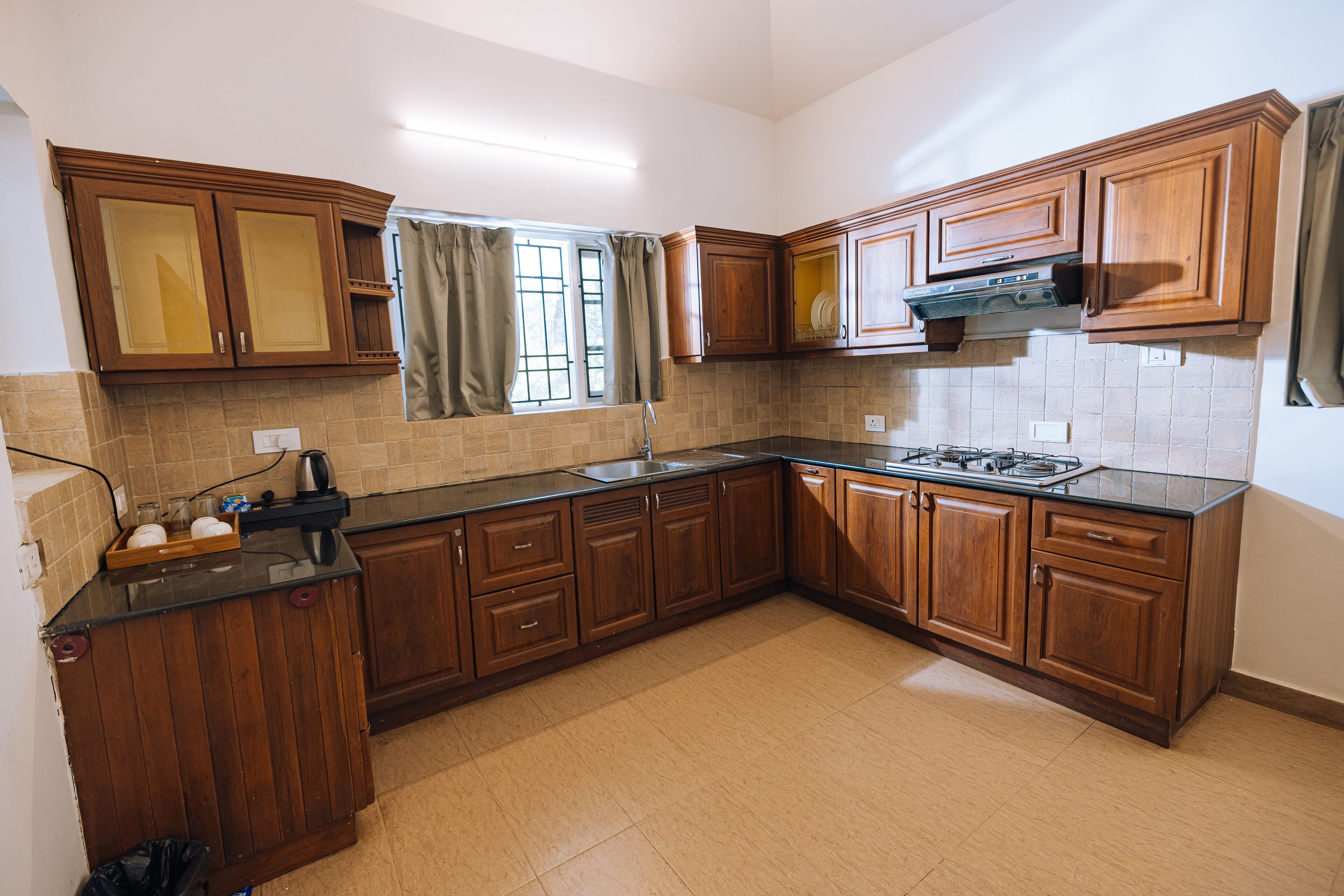 A kitchen with wooden cabinets, a black countertop, a window with curtains, and a tiled backsplash.