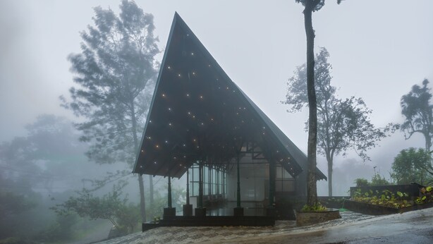 A modern building with a triangular roof and large windows, surrounded by trees and fog. - ELIXIR WOODS RESORT AND SPA (Devikolam)
