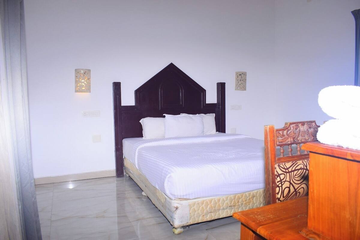 A bedroom with a bed, a wooden headboard, a nightstand, and a wall-mounted light fixture.