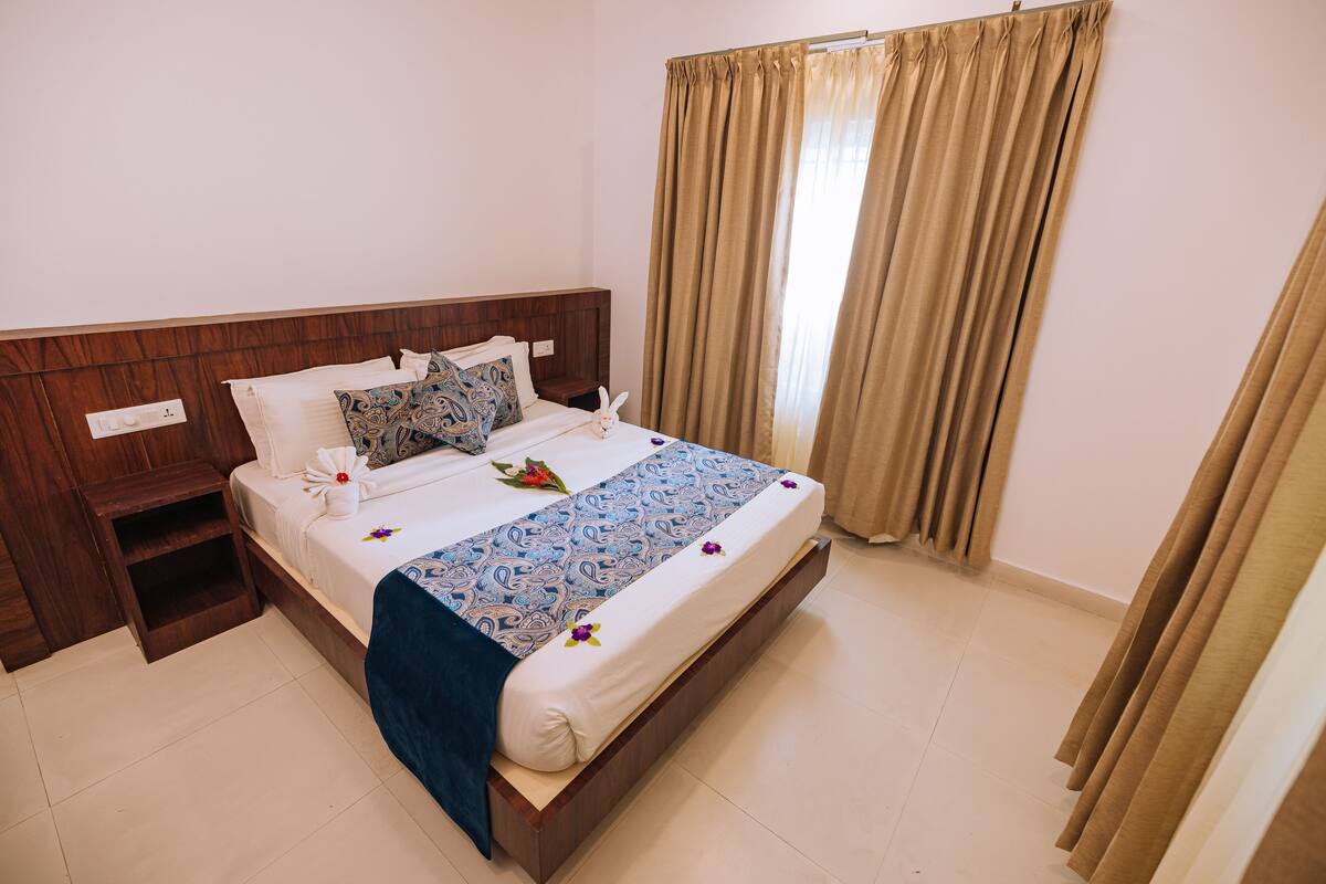 A neatly made bed with a blue patterned bedspread, a wooden headboard, and a bedside table with a lamp.