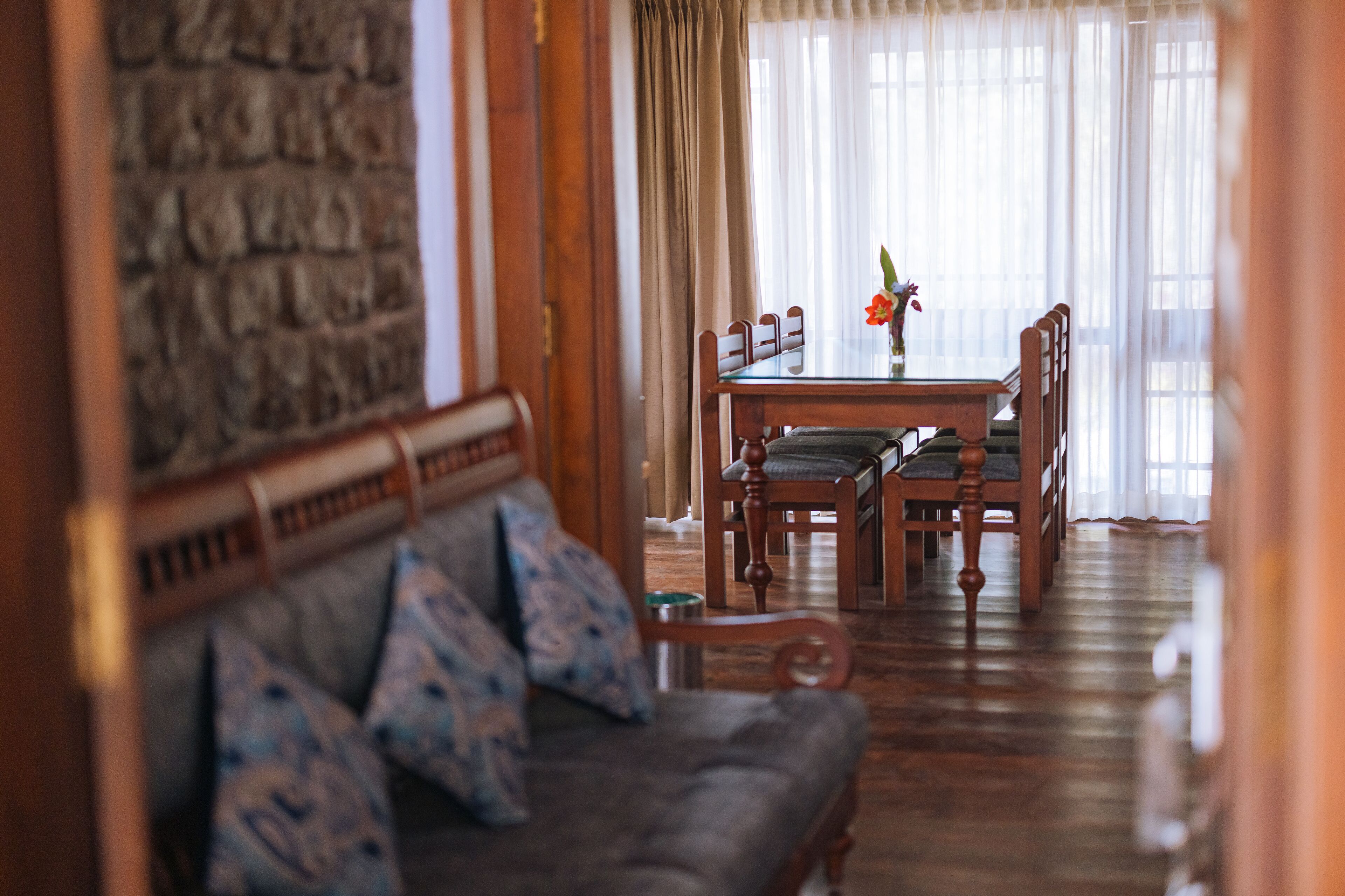 A cozy living room with a wooden sofa, a dining table with chairs, and a stone wall.
