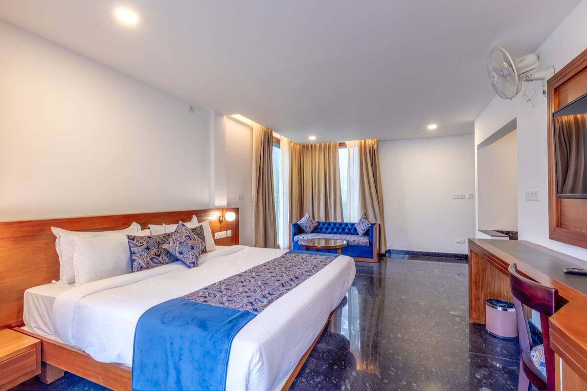A hotel room with a large bed, a sofa, a desk, and a mirror.