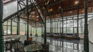 A spacious indoor area with a glass ceiling, metal railings, and a seating area with benches and tables. - ELIXIR WOODS RESORT AND SPA (Devikolam)