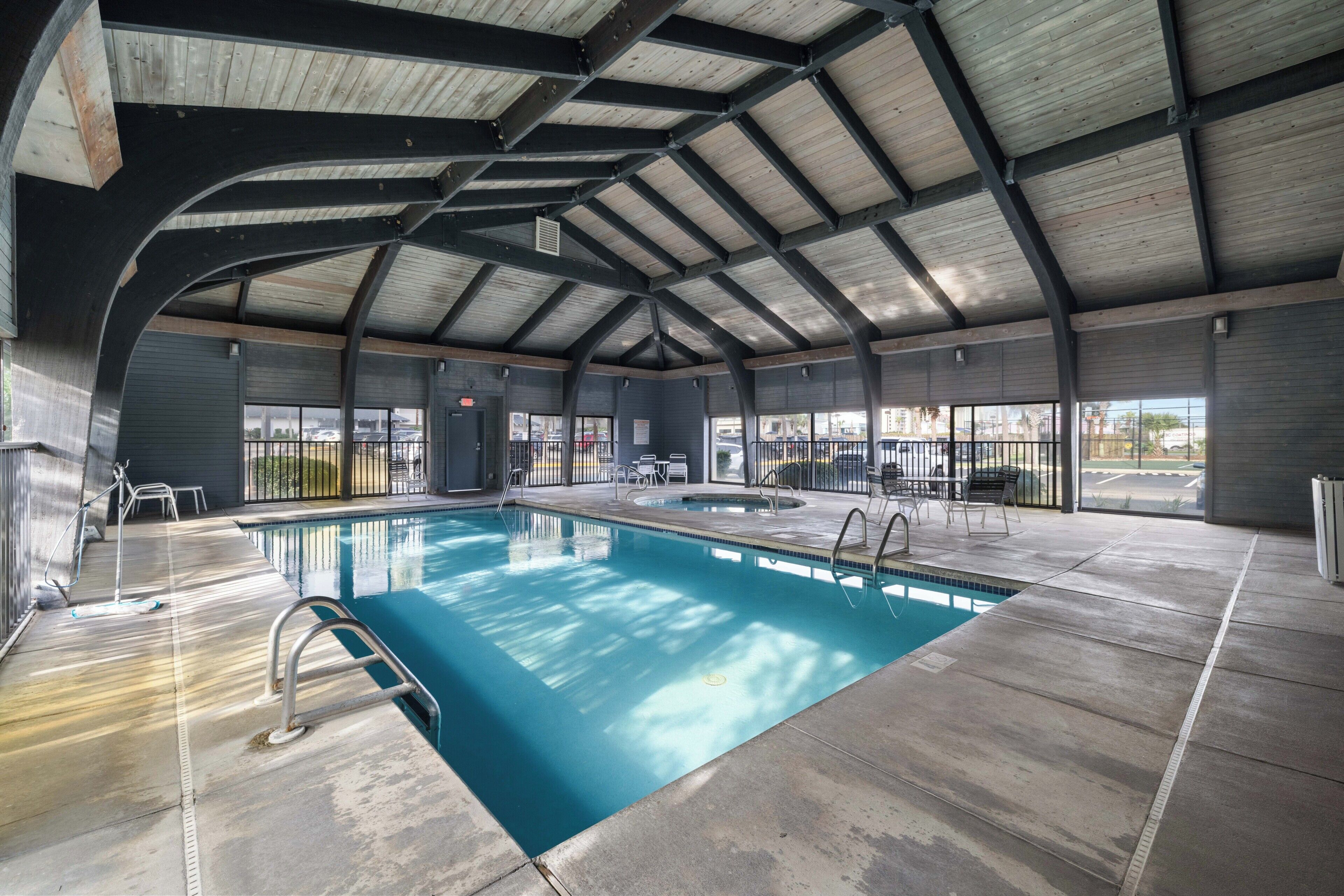 An indoor swimming pool with a high ceiling, clear glass walls, and a concrete floor.