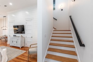 Ein modernes Interieur mit einer Holztreppe, weißen Wänden und einem flachbildfernseher, der über einem weißen Schrank angebracht ist.