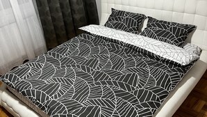 A bed with a geometric patterned bedspread and pillows, a tufted headboard, and a wooden parquet floor. - Apartament la 3 minute de aeroport, in centrul orasului langa parc si restaurant (Otopeni)