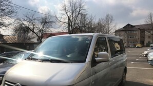 A silver van parked in a lot with buildings and leafless trees in the background. - Apartament la 3 minute de aeroport, in centrul orasului langa parc si restaurant (Otopeni)