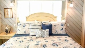 Un lit avec une tête de lit, plusieurs oreillers et une couvre-lit ornée d’un motif sur le thème de la mer.