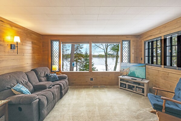 A cozy living room with a large window, a flat-screen TV, and a comfortable sofa.