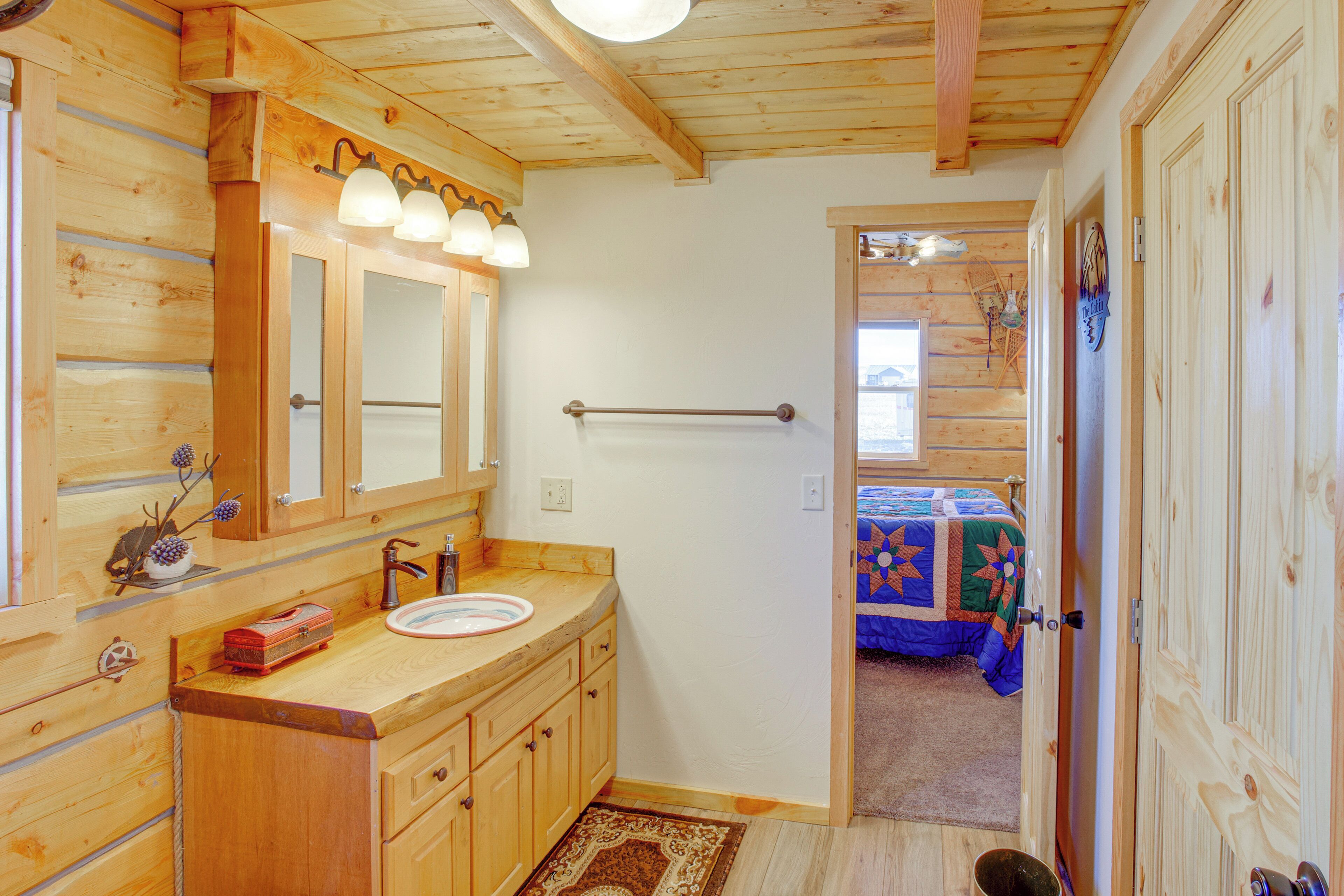 A wooden cabin interior with a bathroom, a sink, and a door leading to a bedroom.