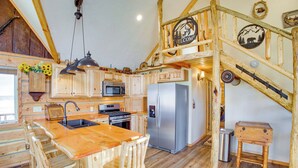 Una cocina rústica con armarios de madera, un refrigerador de acero inoxidable y una isla de madera con taburetes de bar.