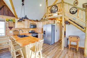 A rustic kitchen with wooden cabinets, a stainless steel refrigerator, and a wooden island with bar stools. - Roberts Home w/ Western Decor & Mountain Views! (Roberts)