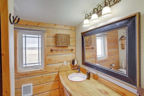 Une salle de bain rustique, avec des murs en bois, un grand miroir, une fenêtre et un lavabo.