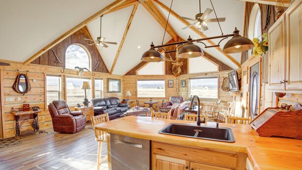 Una cabaña de madera espaciosa con isla de cocina, comedor de madera y un ventanal con vistas a un paisaje pintoresco.