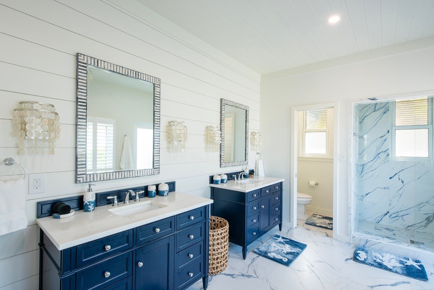 Une salle de bain moderne avec deux vasques, des meubles bleu foncé et un espace de douche en marbre.