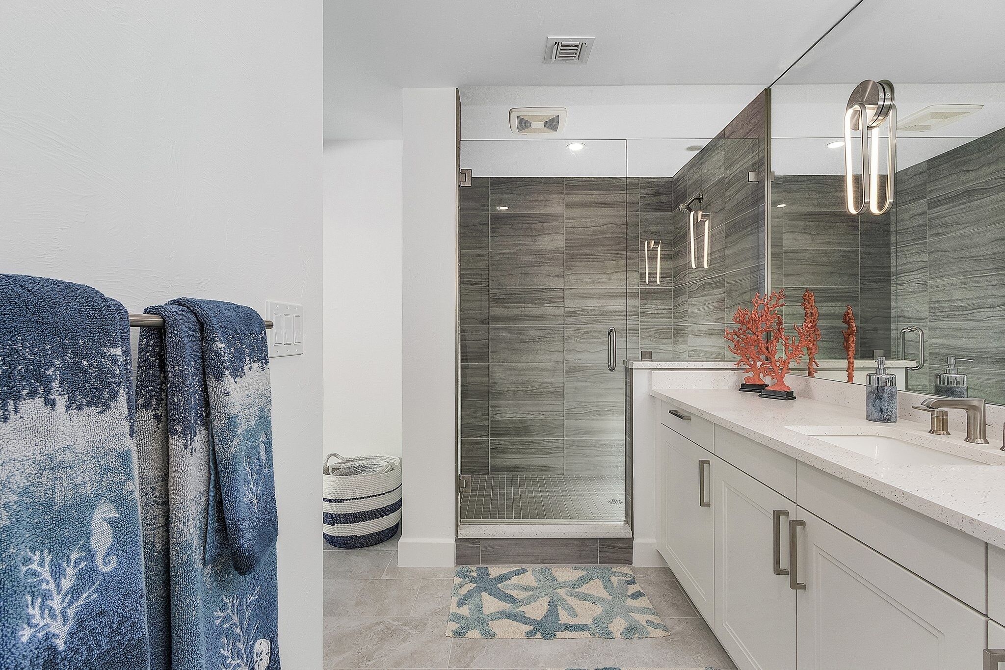 A modern bathroom with a glass shower enclosure, a large mirror, and a white vanity with a sink and towel rack.