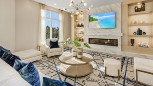 A modern living room with a round coffee table, a sofa, a TV mounted on the wall, and a fireplace. - Grandview #603 - 4142 Bay Beach Ln 3 Bedroom Condo by RedAwning (Fort Myers Beach)