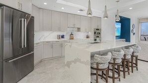 A modern kitchen with a large island, stainless steel appliances, and bar stools. - Grandview #603 - 4142 Bay Beach Ln 3 Bedroom Condo by RedAwning (Fort Myers Beach)