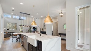 Una cocina moderna con una isla grande, iluminación colgante y vistas al salón.