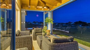 A modern outdoor seating area with wicker furniture and a glass enclosure, overlooking a residential area at dusk. - Luxurious home in Fazana (Fazana)