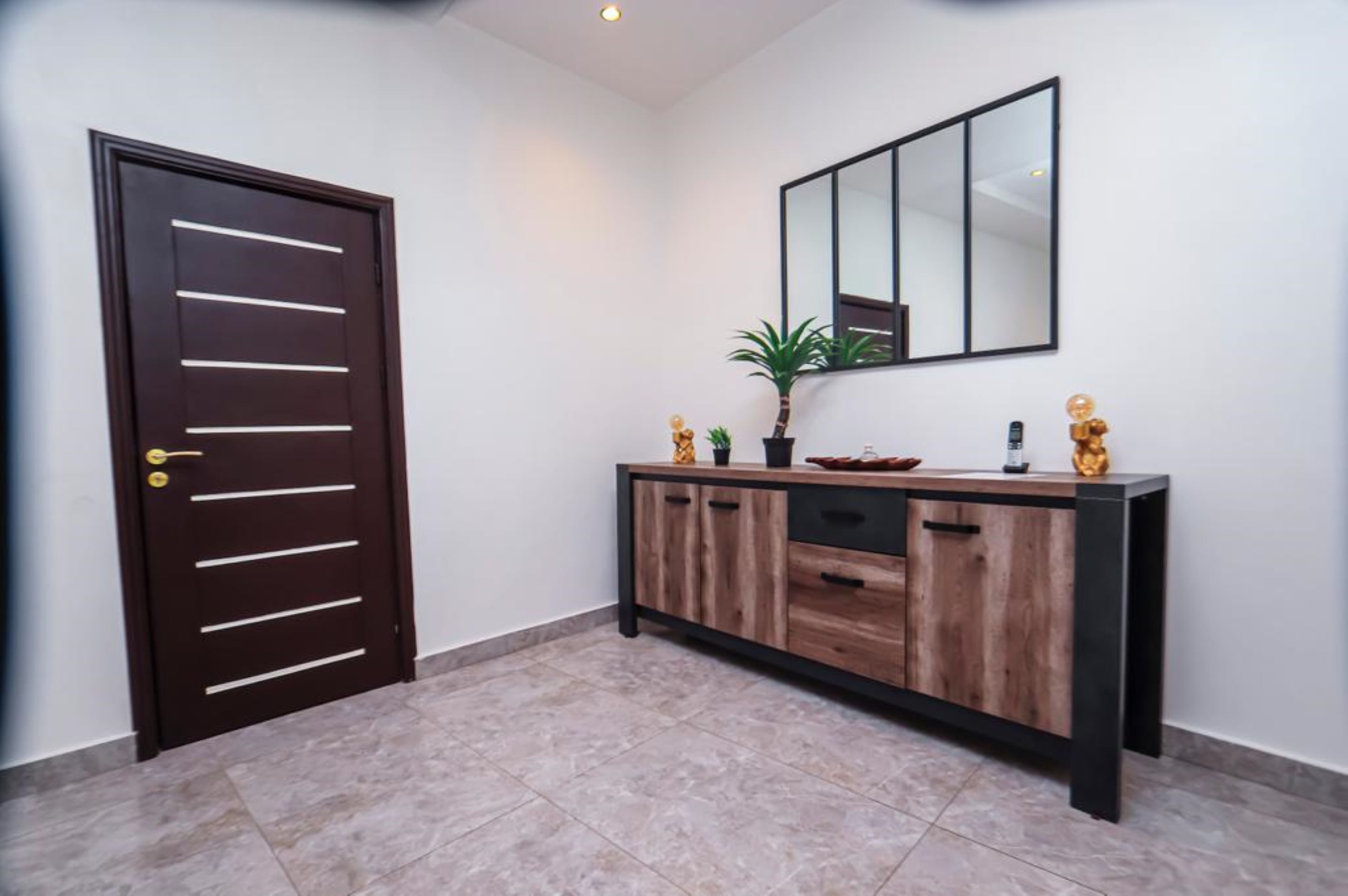 Un pasillo con una puerta de madera oscura, una consola con un espejo y una planta en maceta.