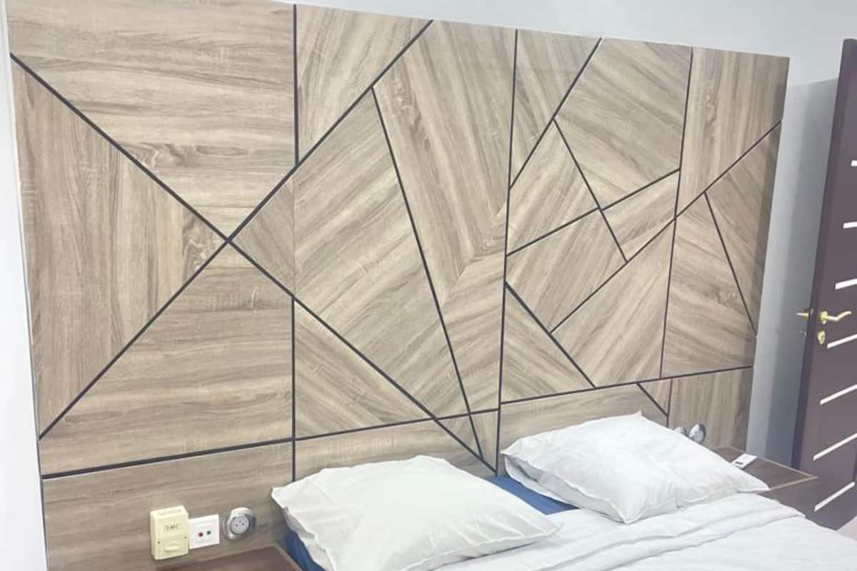 A bedroom with a modern geometric headboard, a wooden nightstand with a drawer, and a bed with white bedding.