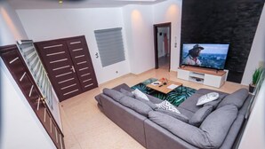 Moderni olohuone, jossa on harmaa sohva, litteänäyttöinen televisio ja puinen sohvapöytä.