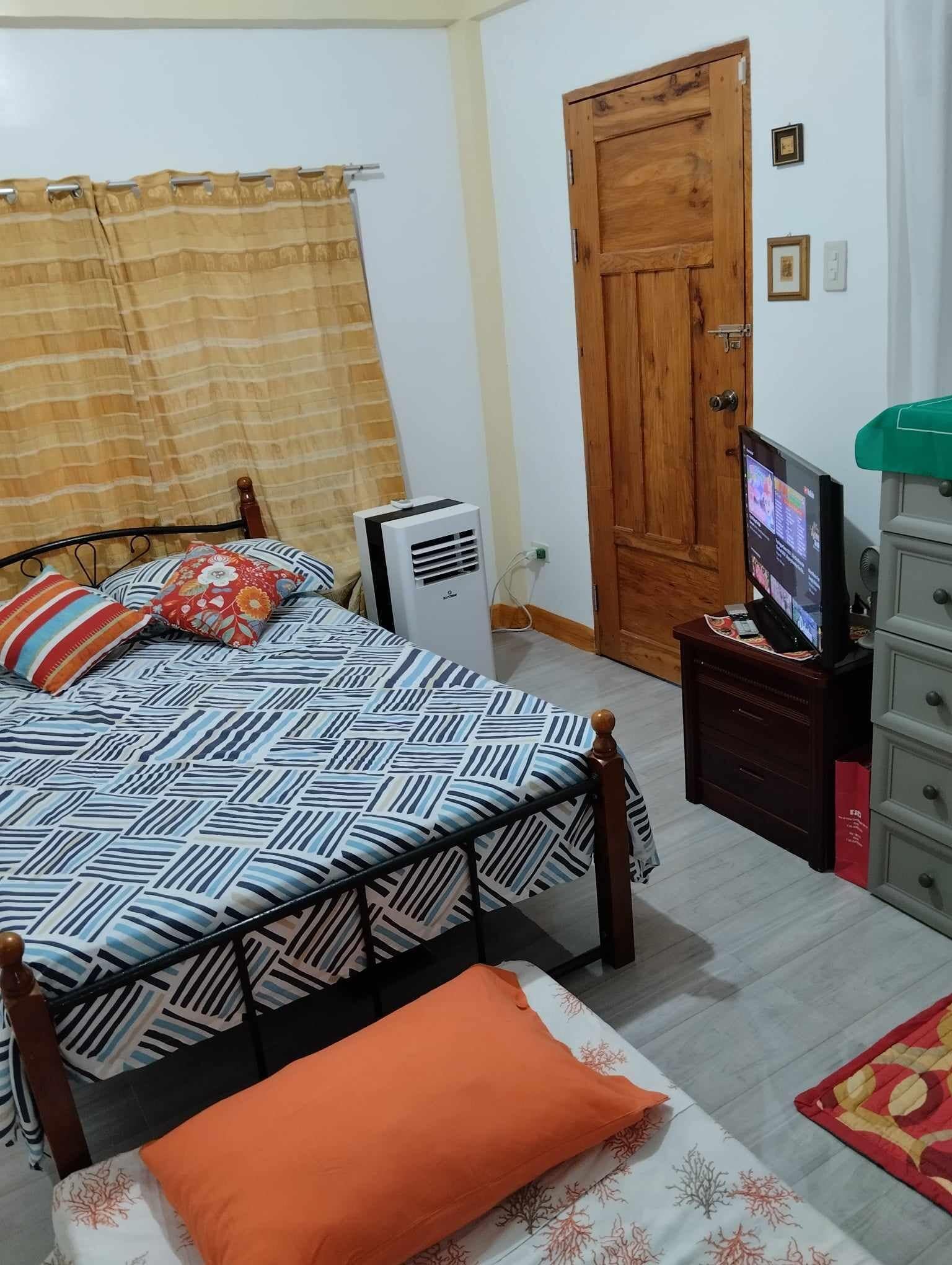 Un dormitorio con cama, puerta de madera, televisor y cómoda.