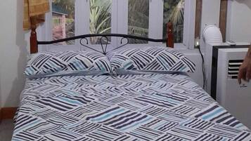 Un letto con copriletto decorato, una finestra con tende e un condizionatore d'aria fissato al muro.