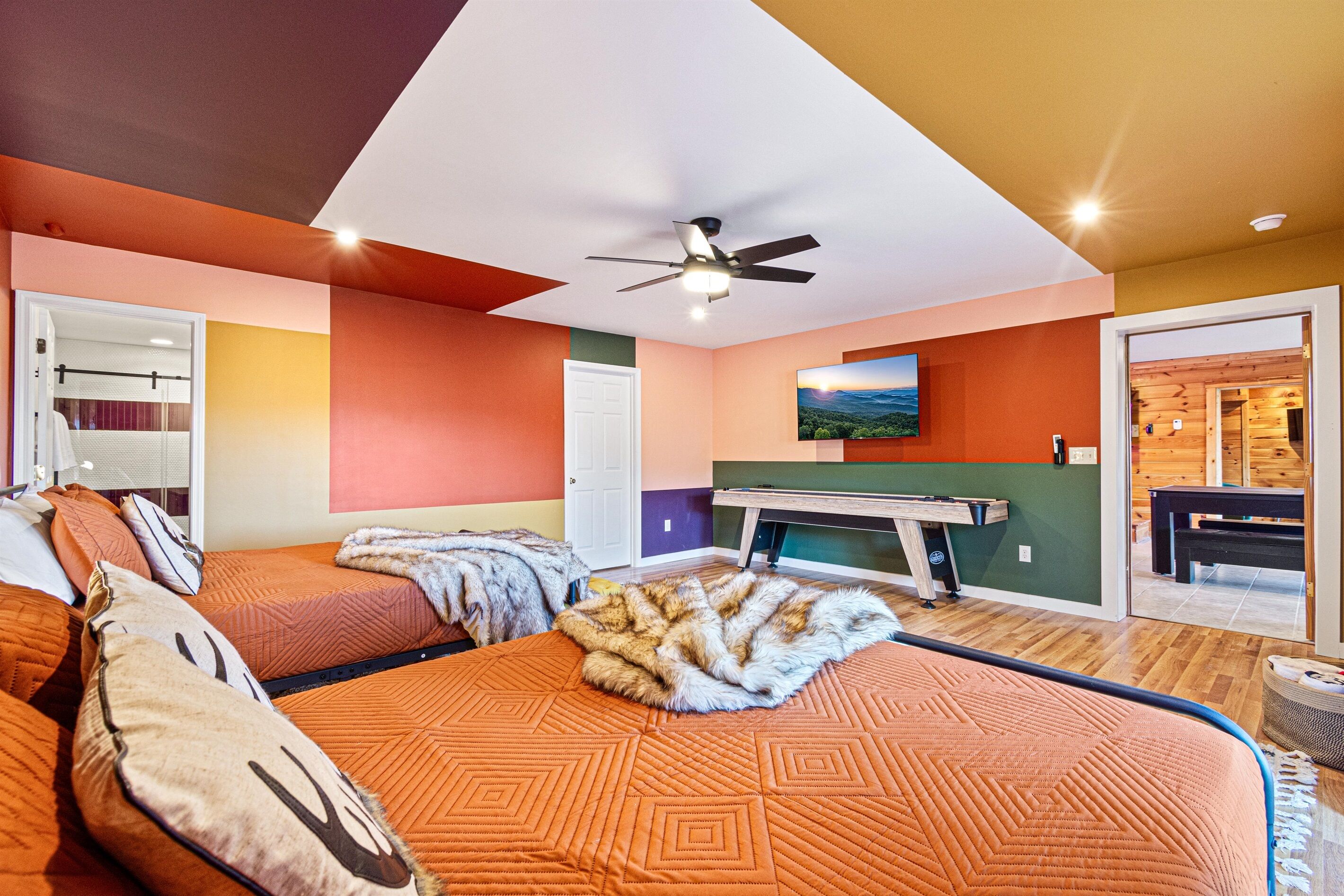 A bedroom with a bed, pillows, a blanket, a ceiling fan, a door, and a view of a pool table and outdoor area.