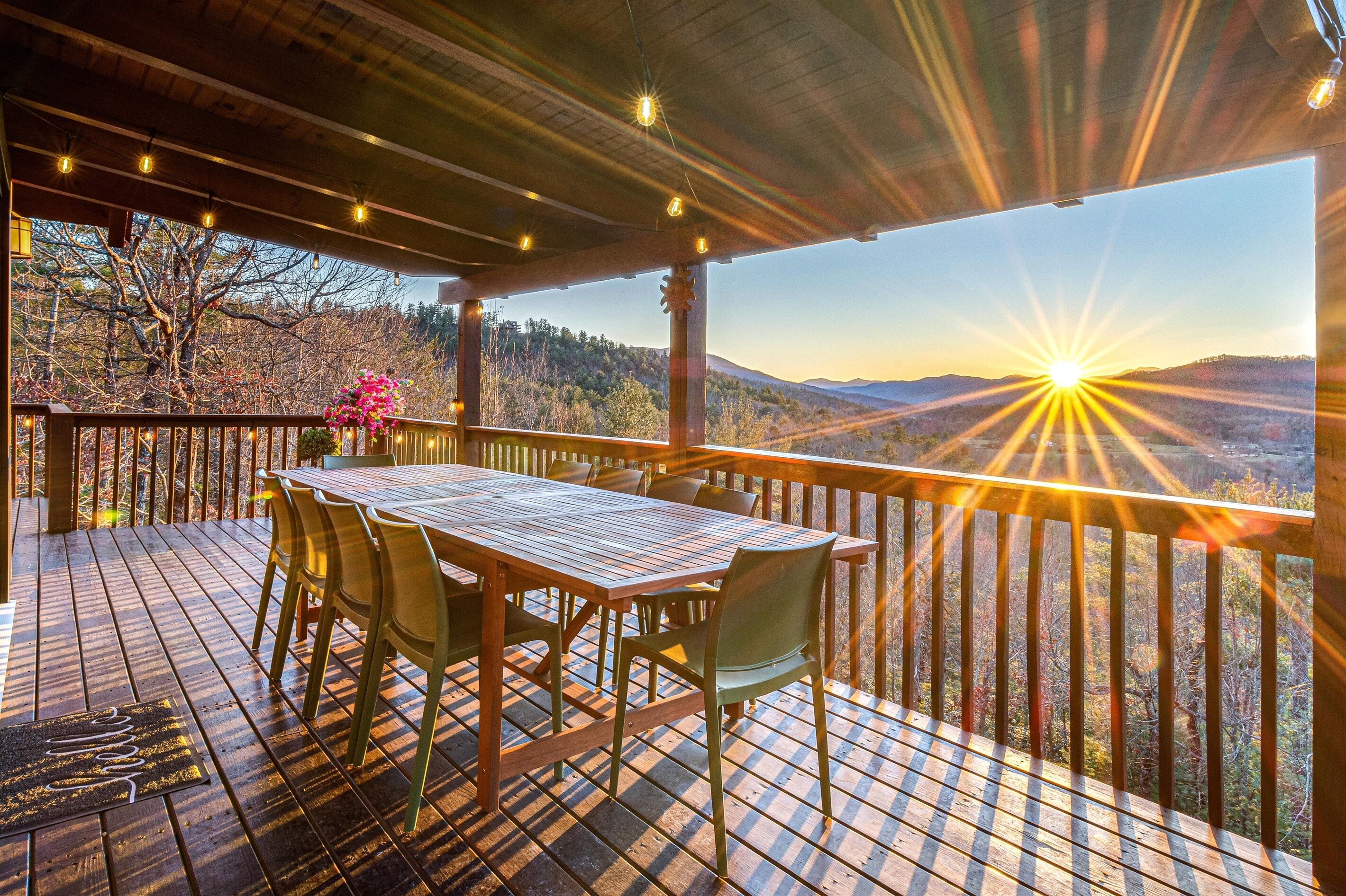 Une terrasse en bois avec une table et des chaises, offrant une vue panoramique sur un paysage magnifique, avec des montagnes et un ciel dégagé.