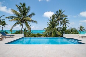 Una piscina con agua azul cristalina, rodeada de palmeras y vista al océano.
