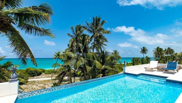 Une piscine d’eau cristalline, d’un bleu éclatant, avec vue sur l’océan et les palmiers.